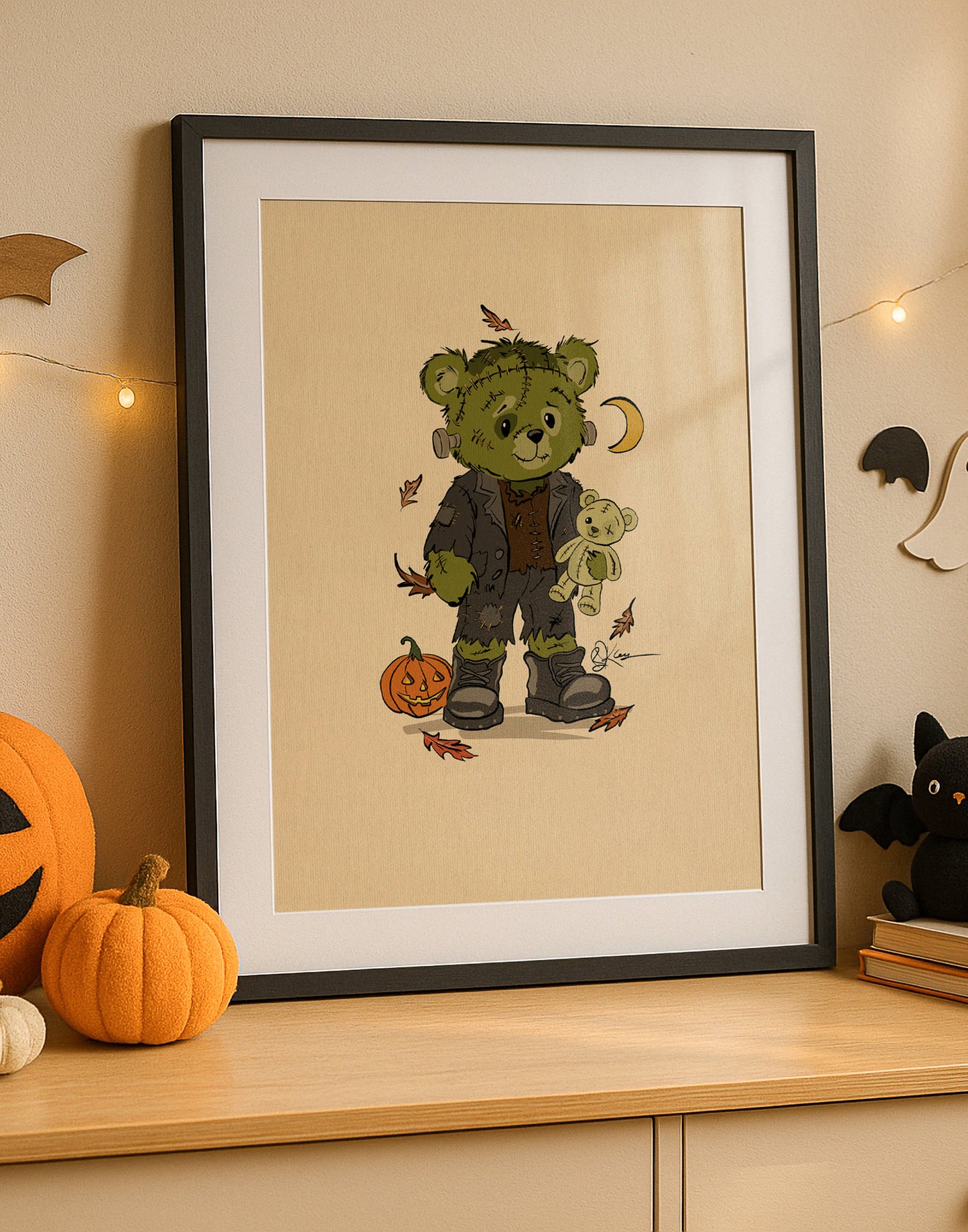 A framed print from The Pola Bears Halloween 2025 Collection, featuring the limited edition print Fred. The print shows a Pola Bear dressed as Frankenstein's monster, holding a small teddy bear. The bear is standing next to a carved jack-o'-lantern with autumn leaves scattered around its feet. The framed print sits on a wooden cabinet, with a pumpkin and bat and ghost decorations in the background.