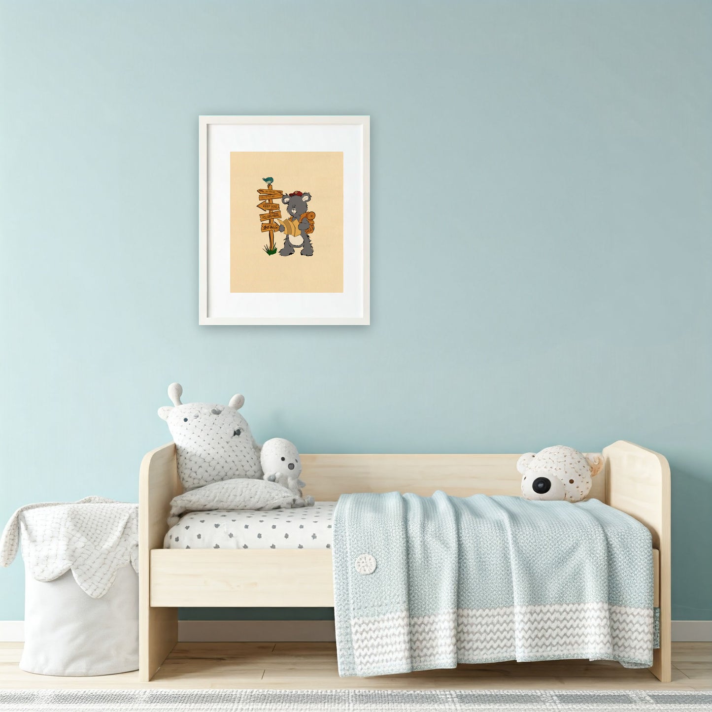 Framed Pola Bear Peter nursery print above a light wood toddler bed with blue bedding and plush animal toys, styled against a calming blue wall for a serene kids' room look.