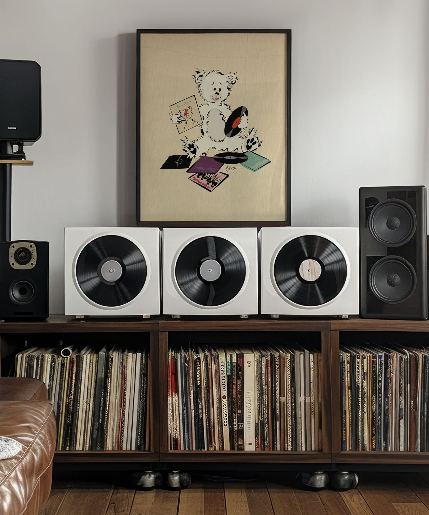 A framed print of a whimsical Pola Bear with its ears cocked, holding a record. On the floor in front of it are several album covers. The art hangs above a stereo console featuring three large white record-player-like devices with speakers on either side. Below the console are two shelves filled with vinyl records.