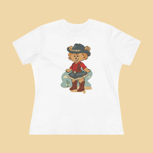White women's fitted t-shirt featuring a whimsical illustration of Laverne the Pola Bear dressed as a cowgirl, wearing a cowboy hat, red western shirt, denim skirt, and boots.