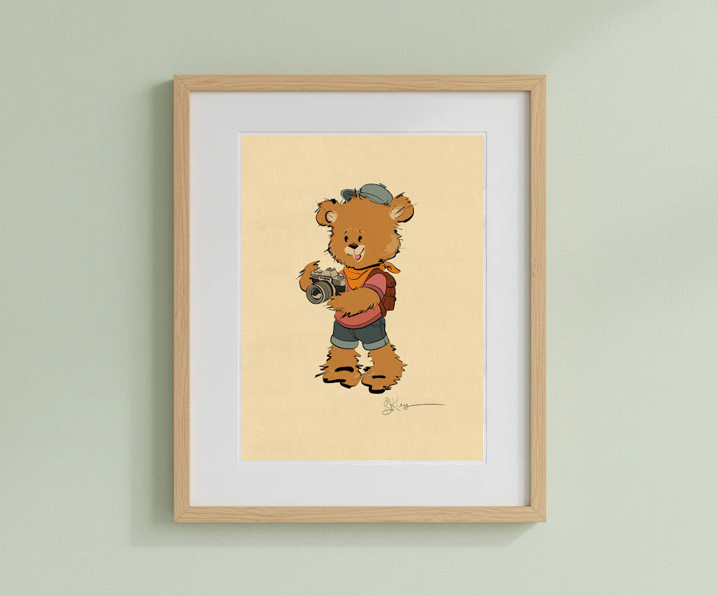 Framed art print featuring the vintage-style illustration of Isaac, the Pola Bear character with a camera, in a light wood frame with a white mat, hanging on a light green wall.
