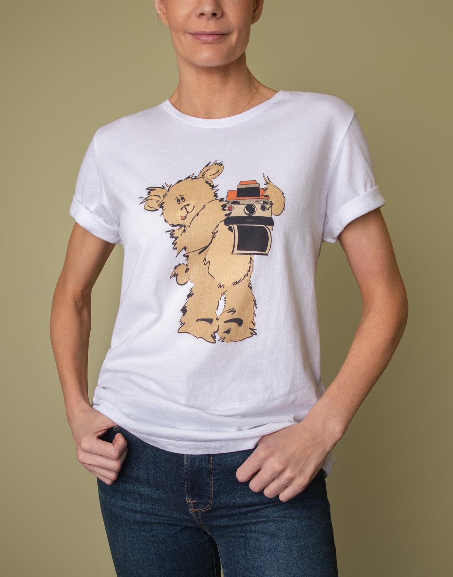 Model wearing a white women's crewneck t-shirt featuring a whimsical illustration of Greg the Pola Bear holding a vintage camera.