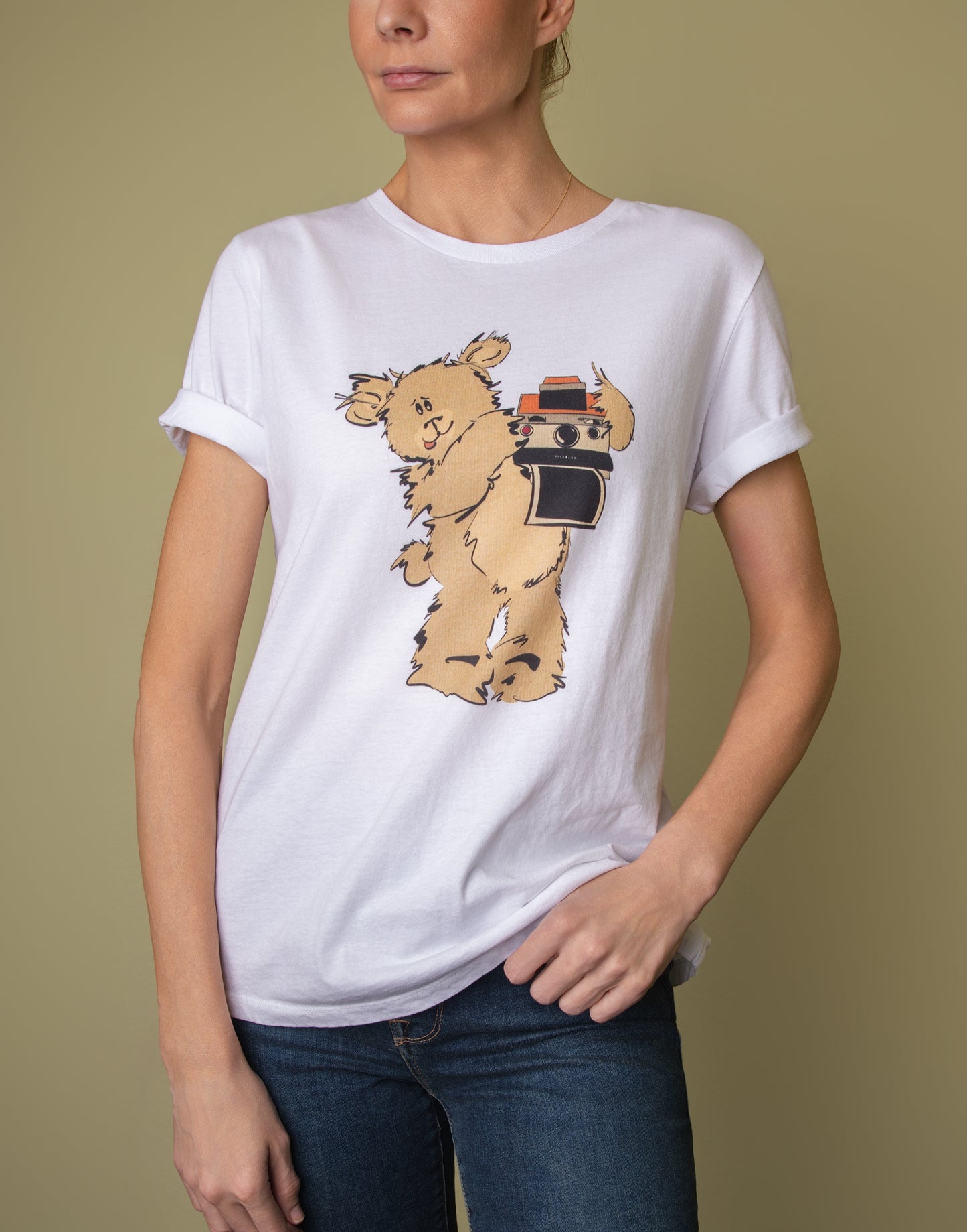 Model wearing a white graphic tee styled with rolled sleeves, featuring a print of Greg the Pola Bear holding a camera.